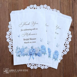 Personalized blue hydrangea bridal shower favor bags, larger than most these bags are perfect for sweet treats including cookie bars or candy buffets.  White bags adorned with delicate blue hydrangeas and butterflies, these will add a touch of elegance to your event.  Printed with 'Thank you for celebrating with us' brides name and event date.