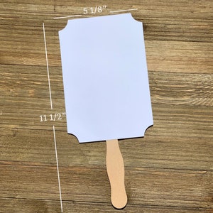 K&ouml;nnte beinhalten: Wei&szlig;es, leeres Schild mit gewellten Kanten, das an einem Holzgriff befestigt ist. Das Schild ist 29,2 cm hoch und 13 cm breit.