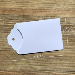 May include: White envelope with a scalloped edge and a hole for a string. The envelope measures 5 3/4 inches by 3 3/8 inches.