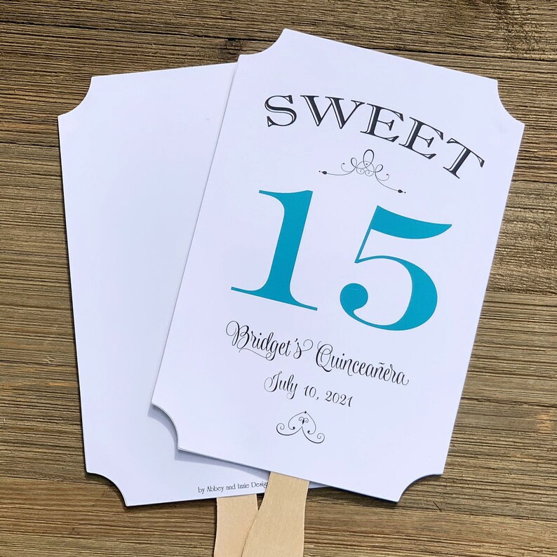 Op de afbeelding: Een witte en turquoise blauwe papieren waaier met de tekst "SWEET 15 Bridget's Quincea&ntilde;era July 10, 2021" en een decoratief ontwerp.
