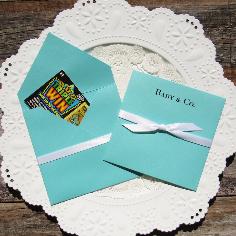 Tiffany Blue baby shower favors, personalized for the new baby.  Each is printed on tiffany blue card stock with a white ribbon tied around, slide a lottery ticket in for a fun and easy baby shower favor.