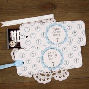 K&ouml;nnte beinhalten: Zwei blaue und wei&szlig;e Geschenkanh&auml;nger mit einem Kreuzmuster und einem blauen Kreis mit dem Text "RIVER'S BAPTISM 08.07.21" und einem Kreuz darin. Die Anh&auml;nger sind mit blauem und wei&szlig;em Band gebunden.