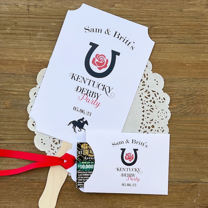 May include: A white card with black text and a red rose in a black horseshoe. The text reads "Sam & Britt's Kentucky Derby Party 05.06.23". A black horse and jockey are pictured at the bottom of the card.