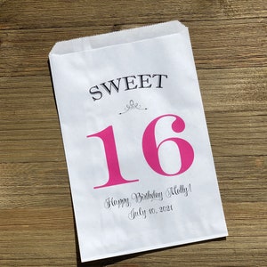 Op de afbeelding: Witte papieren traktatiezak met de woorden "SWEET 16" in zwart en roze. De zak bevat ook de tekst "Happy Birthday Molly! July 10, 2021" in een scriptlettertype. De zak ligt op een houten oppervlak.
