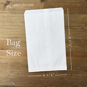 May include: A white paper bag with the text "Bag Size" and measurements of 9 1/4" high and 6 1/4" wide. The bag is rectangular and has a folded top. The background is a wooden surface.