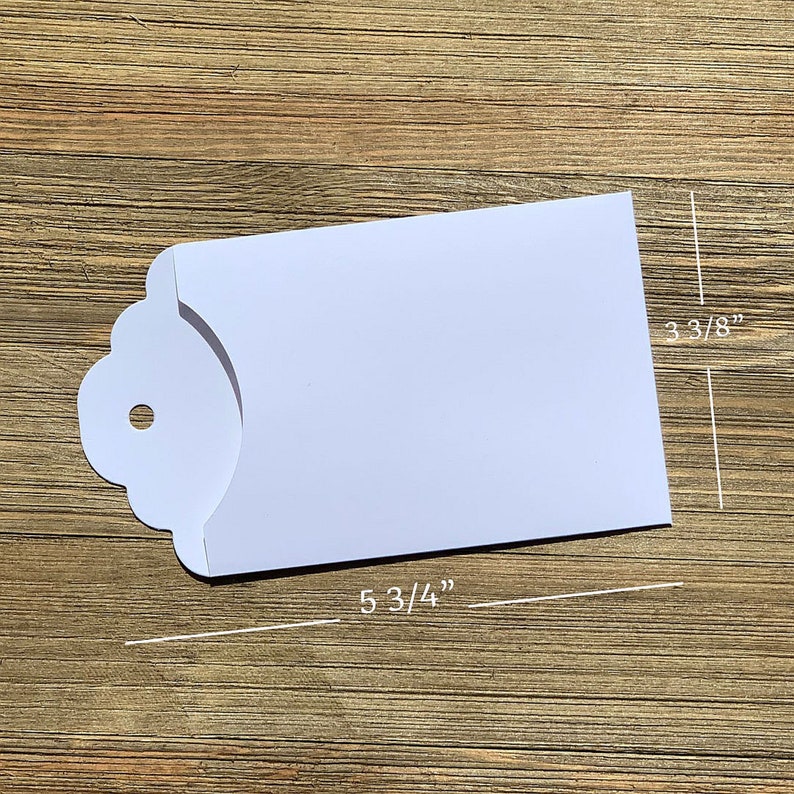 May include: White envelope with a scalloped edge and a hole for a string. The envelope measures 5 3/4 inches by 3 3/8 inches.