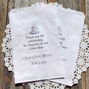 K&ouml;nnte beinhalten: Wei&szlig;e Papier-Geschenkbeutel mit einer blauen und grauen Lamm-Illustration. Die Beutel haben den Text "Vielen Dank f&uuml;r die Feier der Taufe unseres kleinen Mannes Jaxon Chase Hilton am 27. Juni 2021".