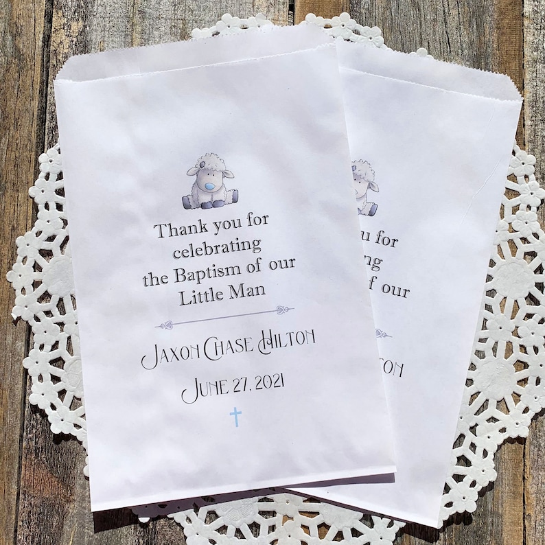 K&ouml;nnte beinhalten: Wei&szlig;e Papier-Geschenkbeutel mit einer blauen und grauen Lamm-Illustration. Die Beutel haben den Text "Vielen Dank f&uuml;r die Feier der Taufe unseres kleinen Mannes Jaxon Chase Hilton am 27. Juni 2021".