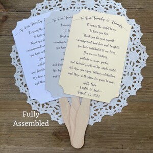 May include: Three wedding fan programs with ivory, white, and gray paper. The text on the ivory program reads "To Our Family & Friends It means the world to us to have you here. Thank you for your support, encouragement and love and laughter you have contributed to our lives. You are our teachers, partners in crime, guides and favorite people in the whole world. We hope you enjoy today's celebration and these we'll share for years to come. With love, Kristen & Jack August 13, 2022"