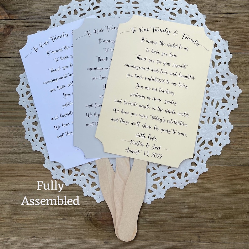 May include: Three wedding fan programs with ivory, white, and gray paper. The text on the ivory program reads "To Our Family & Friends It means the world to us to have you here. Thank you for your support, encouragement and love and laughter you have contributed to our lives. You are our teachers, partners in crime, guides and favorite people in the whole world. We hope you enjoy today's celebration and these we'll share for years to come. With love, Kristen & Jack August 13, 2022"