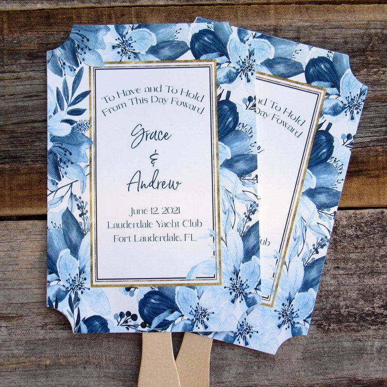May include: Blue and white floral wedding fans with gold trim. The fans have the text "To Have and To Hold From This Day Forward Grace & Andrew June 12, 2021 Lauderdale Yacht Club Fort Lauderdale, FL" printed on them.