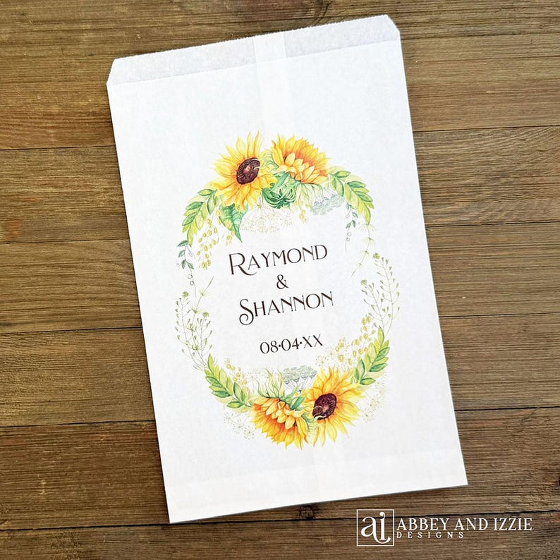 Pode incluir: Saco de papel branco com um design floral com girass&oacute;is e vegeta&ccedil;&atilde;o. O saco tem os nomes "Raymond & Shannon" e a data "08-04-XX" impressos. O saco &eacute; da Abbey and Izzie Designs.