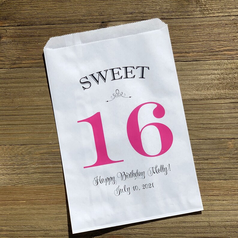 Op de afbeelding: Witte papieren traktatiezak met de woorden "SWEET" en een grote roze "16" op de voorkant. Daaronder staat de tekst "Happy Birthday Molly! July 10, 2021". De zak ligt op een houten oppervlak.