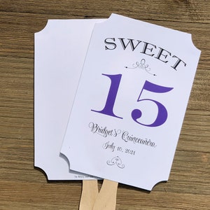 Op de afbeelding: Een witte en paarse waaier met de tekst "SWEET 15 Bridget's Quincea&ntilde;era July 10, 2021" en een decoratief swirl-ontwerp.