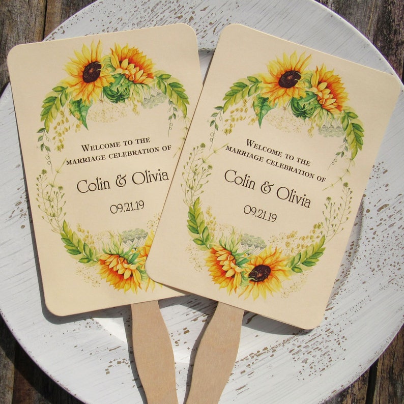 Sunflower wedding fans, personalized for the bride and groom adorned with a circle of sunflowers.  Printed on ivory cardstock with wooden handle hidden between front and back cardstock.  Wedding favor fans come fully assembled.