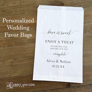 Puede incluir: Una bolsa de papel blanca para recuerdos con el texto "love is sweet" y "Enjoy a treat". La bolsa est&aacute; personalizada con los nombres Alexa & Nathan y una fecha. Tambi&eacute;n son visibles las palabras "Bolsas de recuerdo de boda personalizadas".