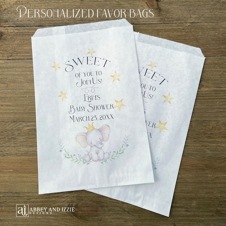 May include: Two white paper favor bags with text and illustrations. The bags read "SWEET OF YOU TO JOIN US!" and "FRINS BABY SHOWER MARCH 23, 20XX". An illustration of a baby elephant with a crown is featured.