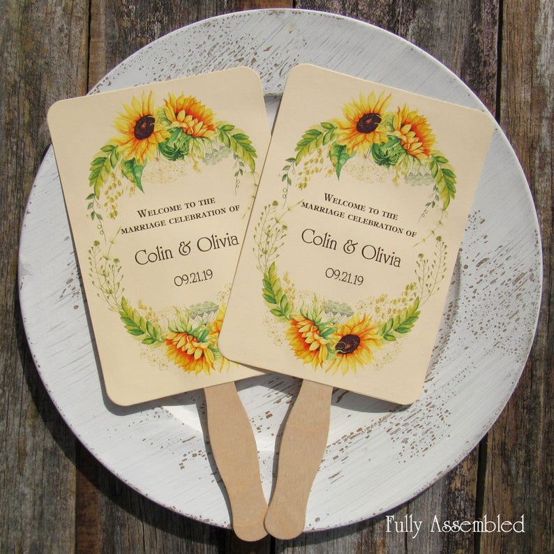 Sunflower wedding fans, personalized for the bride and groom adorned with a circle of sunflowers.  Printed on ivory cardstock with wooden handle hidden between front and back cardstock.  Wedding favor fans come fully assembled.
