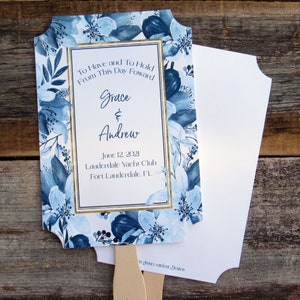 May include: A blue and white floral wedding fan with gold accents. The fan features the text "To Have and To Hold From This Day Forward Grace & Andrew June 12, 2021 Lauderdale Yacht Club Fort Lauderdale, FL".