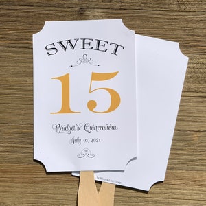 Op de afbeelding: Witte en gouden Quincea&ntilde;era-waaier met de tekst "SWEET 15" en "Bridget's Quincea&ntilde;era July 10, 2021".