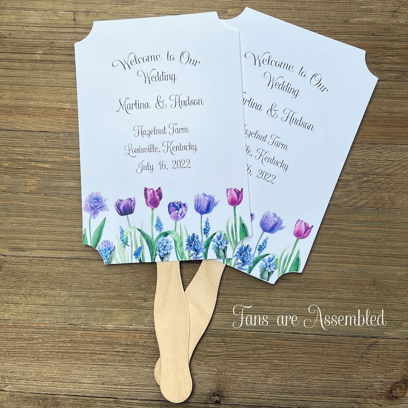 Welcome to our wedding fans adorned with purple tulips for a elegant touch.  Our fans are personalized with the bride and grooms names, wedding place and date.  They are two sided with handle hidden between, printing on one side only, fully assembled