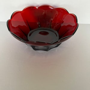 Può includere: Una ciotola di vetro rosso scuro con un bordo a festoni. La ciotola è fatta di vetro trasparente con una tinta rossa.