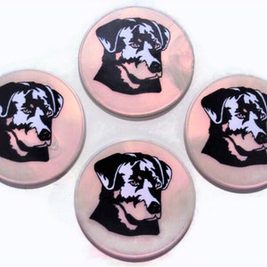 May include: Set of four round coasters featuring a black and white silhouette of a Rottweiler dog's head on a pink iridescent background.