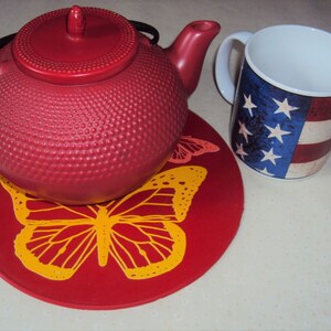 May include: Red teapot with a lid and a handle, sitting on a red coaster with a yellow butterfly design. A white mug with a red, white, and blue American flag design is next to the teapot.