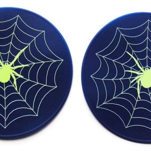 May include: Two round blue coasters featuring a white spider web design with a glow-in-the-dark green spider in the centre.