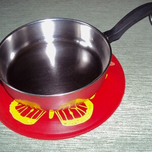 May include: A stainless steel saucepan with a black handle sits on a red silicone hot pad with a yellow butterfly design.