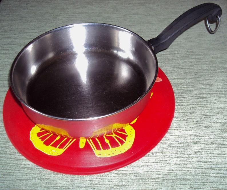 May include: A stainless steel saucepan with a black handle sits on a red silicone hot pad with a yellow butterfly design.