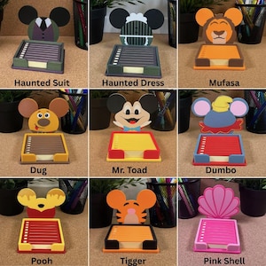 May include: A collection of nine character-themed sticky note holders, each featuring a unique cutout design including Haunted Suit, Haunted Dress, Mufasa, Dug, Mr. Toad, Dumbo, Pooh, Tigger, and a Pink Shell, with colourful paper pads.