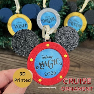 May include: A red circular ornament with black glittery mouse ears and a central blue insert featuring the text Disney MAGIC 2026. The frame includes four yellow circular accents and a white ribbon loop for hanging, designed as a cruise ship porthole.