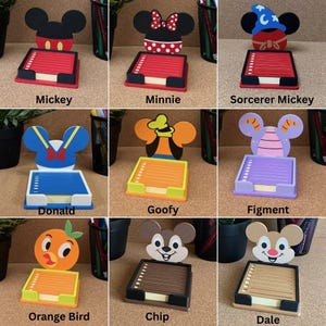 May include: A collection of nine character-themed memo pad holders featuring Mickey, Minnie, Sorcerer Mickey, Donald, Goofy, Figment, Orange Bird, Chip, and Dale. Each holder includes a square base with a stack of paper and a decorative cutout back.