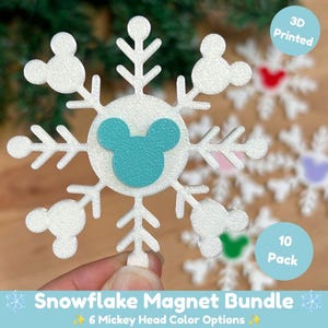 May include: A white 3D printed snowflake magnet featuring a teal Mickey Mouse head icon at the center and smaller Mickey head icons at the tips of the snowflake branches. The text 3D Printed and 10 Pack appear in blue circles, with Snowflake Magnet Bundle and 6 Mickey Head Color Options at the bottom.