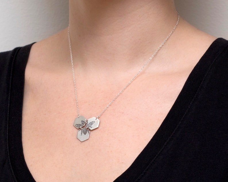 three silver hexagons pendant with etched bee, on a model with white background