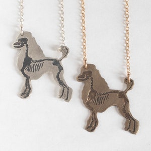 poodle silhouette pendants with etched skeletons- one in brass and one silver. laying together on a white background