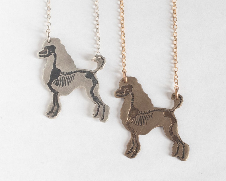 poodle silhouette pendants with etched skeletons- one in brass and one silver. laying together on a white background