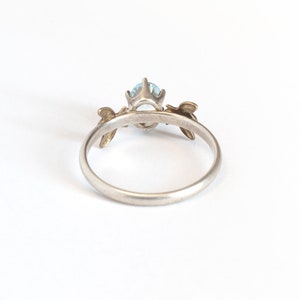 Sky blue oval gemstone ring, in a prong setting with a brass bee on each side. Shown from the back on a white background.