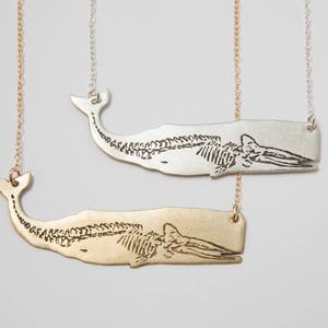 two etched whale skeleton necklaces on a white back ground, one silver and one brass