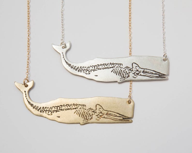 two etched whale skeleton necklaces on a white back ground, one silver and one brass