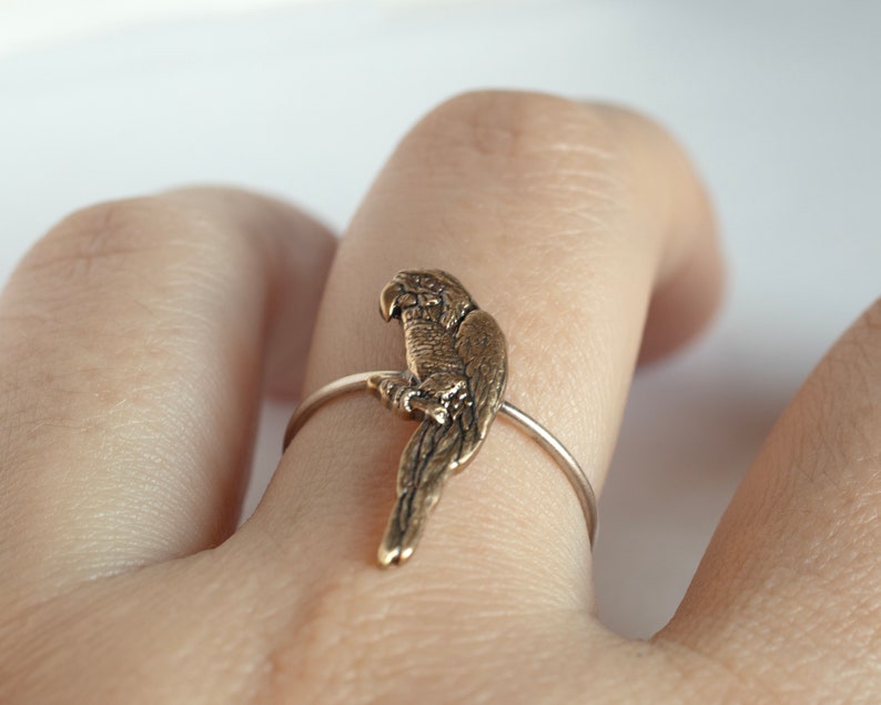 brass parrot charm on a thin silver band. Worn on a hand on a white surface
