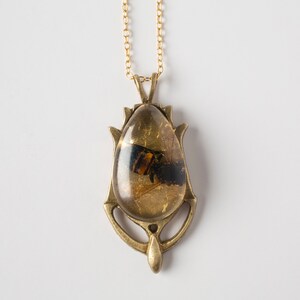 Real honeybee preserved in resin with gold backing in a teardrop shape. Set into a hand carved brass pendant in an art deco style. Shown flat on a white background.