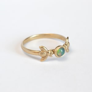 May include: A gold ring with two bee designs and a green opal gemstone in the center.
