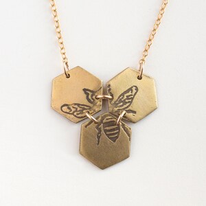 three brass hexagons pendant with etched bee, on white background