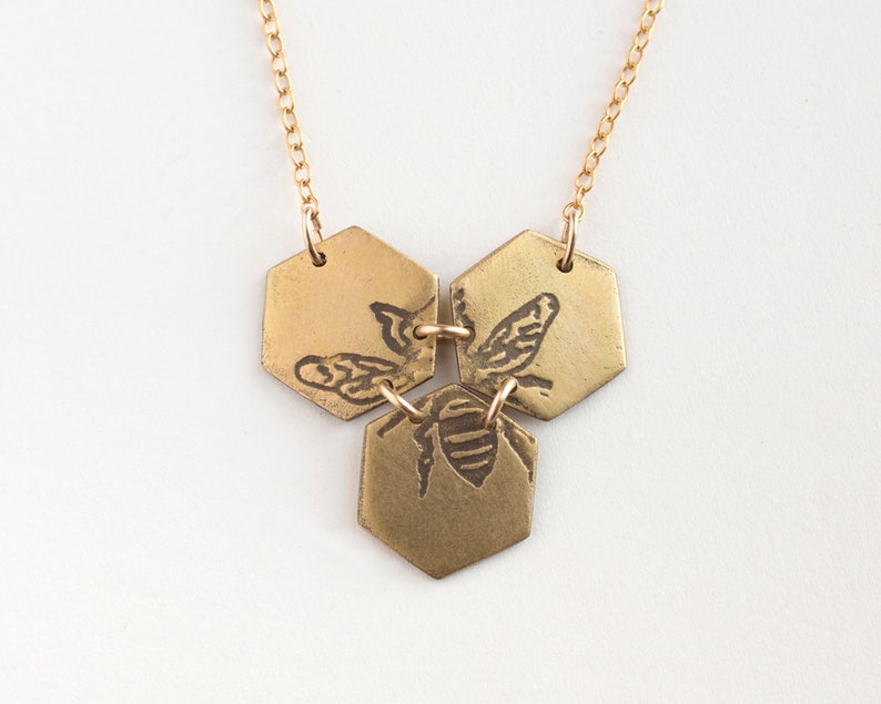 three brass hexagons pendant with etched bee, on white background