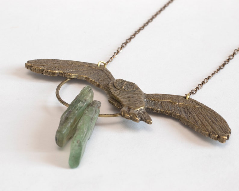 brass barn owl necklace with rough kyanite, at an angle on white background