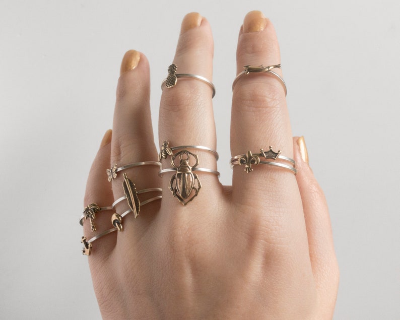 hand held upright wearing many small brass charm rings, in front of a white wall
