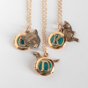 May include: Three gold necklaces with lockets. The lockets feature a cat head, the letter "K" and the letter "D".