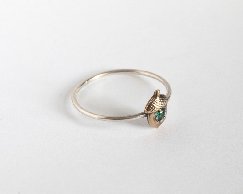 acorn ring with a tiny emerald, at an angle on a white background